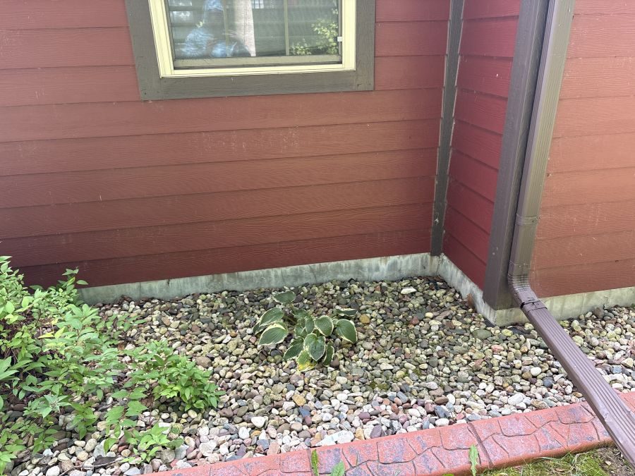 Rock bed and soil grade at an exterior corner, sloping back toward the foundation wall