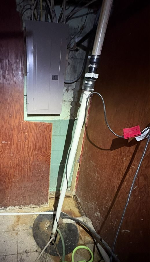 Electrical service panel with a sump pump crock and discharge pipe directly in front of it